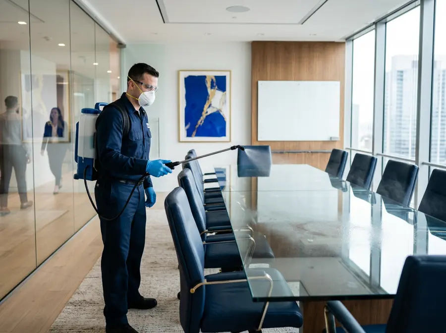 Technician with a backpack electrostatic sprayer treating a conference room